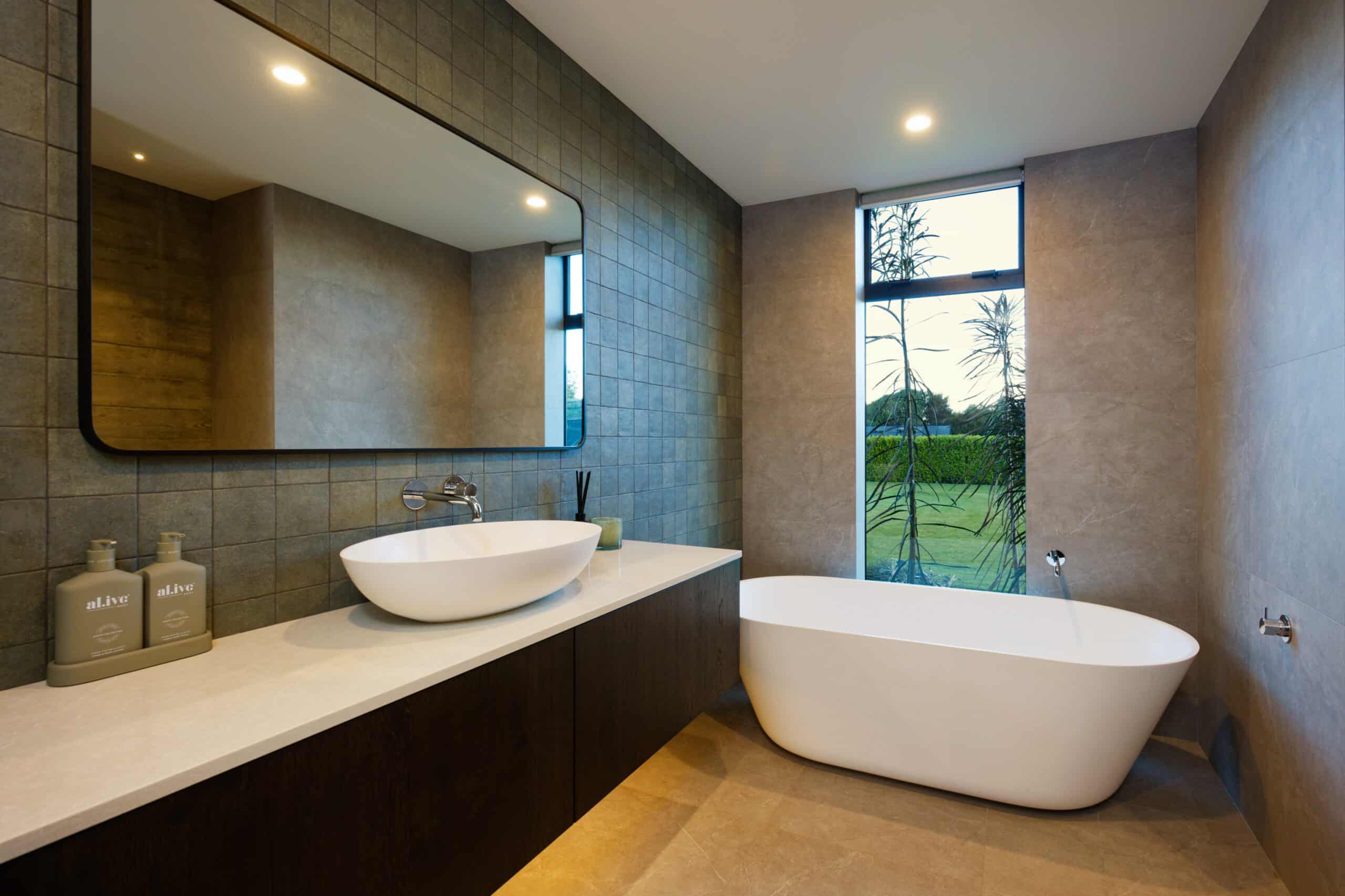 Modern bathroom with freestanding tub, vessel sink, large mirror, and tiled walls. Window view.