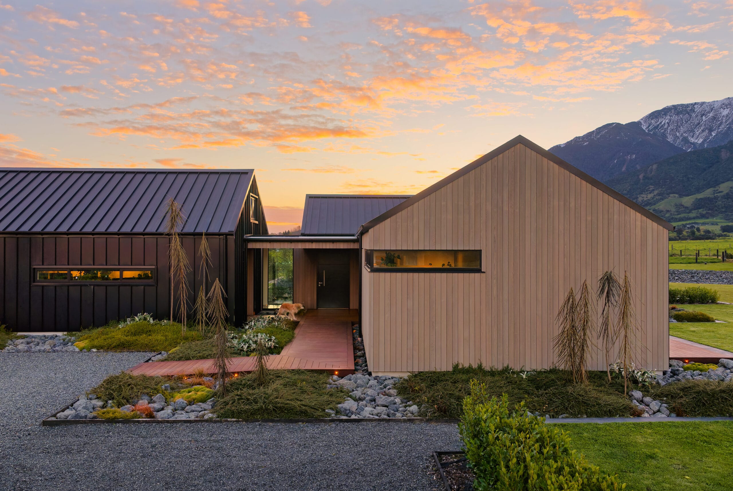 Modern houses with metal roofs at sunset, mountains in background, path and landscaping in front.