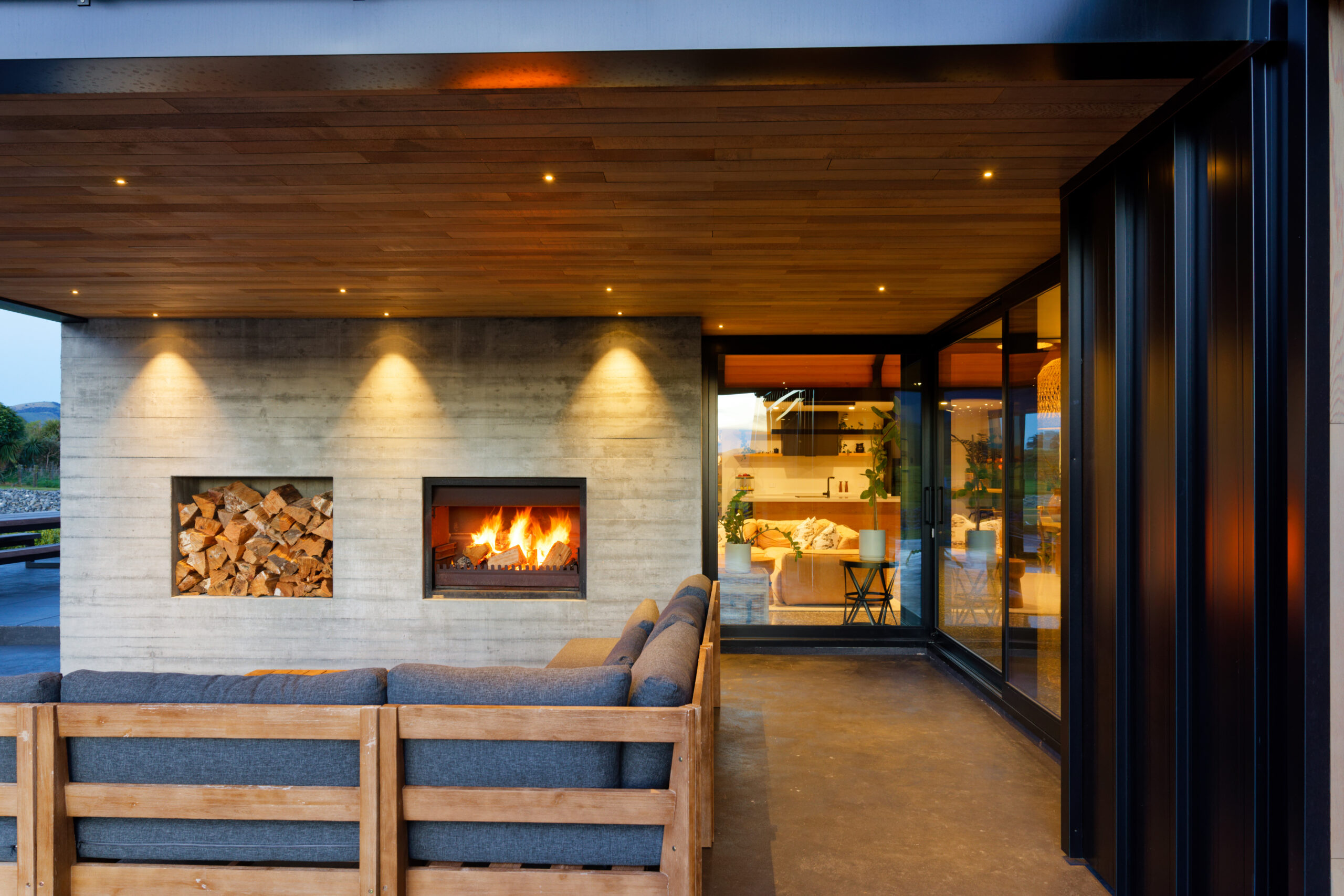 Outdoor living area with built-in fireplace, wood storage, wood ceiling, and glass doors.